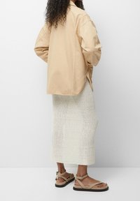 Beige oversized shirt, witte gebreide rok en lichtbruine sandalen met enkelbandjes. Focus op vorm, textuur en kleurcontrasten.