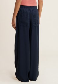 Pantalons à jambe large bleu marine avec une taille élastique, deux poches plaquées à l'arrière et une texture de tissu lisse et léger.
