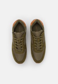 Baskets vert olive avec des matériaux en mesh et en daim, présentant un design à lacets, des accents marron au niveau du talon et des surfaces texturées.