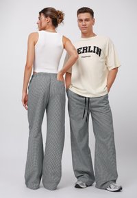 Grå rutig vida byxor med elastisk midja, med sidofickor. Modellerna bär en åtsittande vit linne och en oversized krämfärgad t-shirt.
