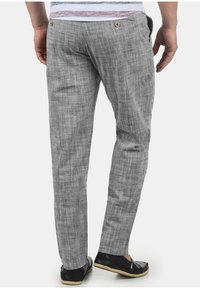 Ljusgrå linbyxor med ett texturerat mönster, med bakfickor och en slim fit-design, bärs tillsammans med svarta slip-on skor.