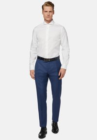 Weißes Hemd mit Knöpfen, blaue Anzughose, schwarzer Gürtel und schwarze Schuhe. Glattes Material, taillierte Passform und lange Ärmel mit geknöpften Manschetten.