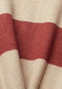 Beige Strickstoff mit weicher Textur und einem breiten roten Streifen. Das Design weist einen sanften Farbkontrast und ein dezentes, warmes Erscheinungsbild auf.