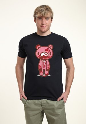 Jonge man draagt een zwart T-shirt met afbeelding van een getroebleerde roze teddybeer met rode vlekken en zichtbaar skelet.