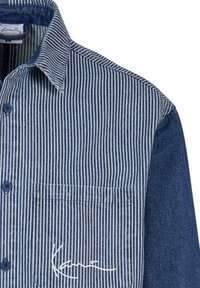 Chemise rayée verticalement bleu et blanc avec manche unie bleu foncé, poche avant avec signature brodée blanche et boutons bleus.