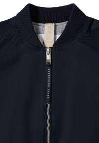 Blouson aviateur bleu marine avec col côtelé, fermeture éclair argentée et texte "CECIL OUTERWEAR" sur la languette de la fermeture éclair.