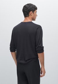 Ciemnoszary sweter z miękkiego materiału, z podwiniętymi rękawami, klasycznym okrągłym dekoltem i luźnym krojem.