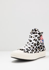 Zapatilla alta con un diseño de estampado de leopardo en blanco y negro, cordones blancos y una suela de goma con un parche de logo rojo y azul.
