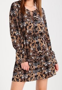 Langärmliges Kleid mit einem schwarz-goldenen Blumendesign, das über einen runden Ausschnitt und ein gestuftes Design verfügt. Aus leichtem Stoff gefertigt.