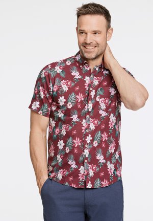 Kortærmet, maroon skjorte med et blomsterprint i pink, hvid og grøn. Har en knaplukning foran og en buet kant.