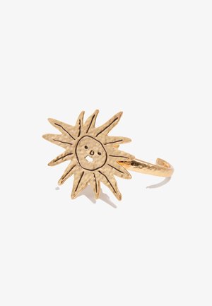 Anillo de tono dorado con un diseño de sol martillado que presenta un rostro simple y rayos grabados en negro sobre un fondo blanco.
