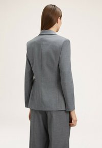 Veste grise sur mesure avec une coupe ajustée, des revers nets et une texture lisse. Dispose d'une fente au dos pour faciliter les mouvements.