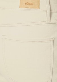 Pantaloni in denim crema con tasca posteriore, cuciture sottili e tessuto testurizzato. Include un'etichetta del marchio in pelle marrone chiaro in vita.