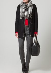 Cappotto di lana nero, maglione rosso, pantaloni grigi su misura, sciarpa houndstooth, borsa nera, stivaletti. Design elegante e moderno con dettagli testurizzati.