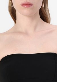 Mustat olkaimettomat topit, joissa on sileä pinta, suora kaula-aukko ja jämäkkä vartalo, täydentää minimalistiset korvakorut.