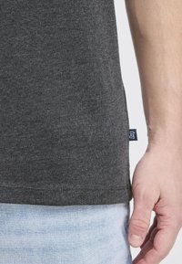 Dunkelgraues Baumwoll-T-Shirt mit Rundhalsausschnitt und kurzen Ärmeln, das ein kleines Markenetikett auf der linken Seite in der Nähe des Saums aufweist.