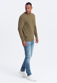 Felpa verde oliva con polsini e orlo a coste, abbinata a jeans skinny blu chiaro e sneaker bianche. Design semplice e casual.