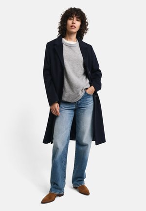 Navy wool coat, gray knit sweater, light blue jeans, brown suede shoes. Features long sleeves, buttons on the coat, and ribbed sweater hem.