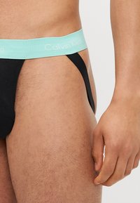 Muška crna tanga donje rublje s svijetloplavim elastičnim pojasom s logom "Calvin Klein", koje pruža čvrsto pristajanje i minimalnu pokrivenost.