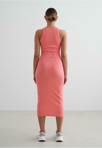 Rochie midi fixă, cu fir ribbat, de culoare roz aprins, cu un design fără mâneci și guler rotund. Asortată cu adidași albi.