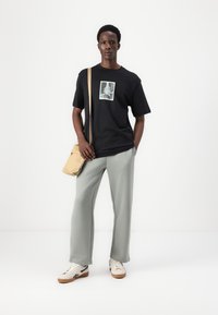 Sort grafisk t-shirt med et trykt billede, parret med lysegrå vidde bukser og hvide sneakers. En beige crossbody taske bæres.