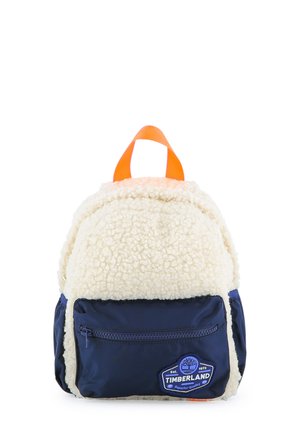 Kleine rugzak met wit, pluizig stof, marineblauw ritsvak aan de voorkant, oranje handvat en Timberland-logo patch.