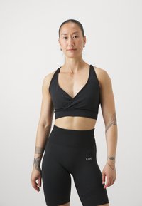 Crni sportski crop top s dubokim V-izrezom i dizajnom s leđa, u kombinaciji s visokim biciklističkim kratkim hlačama koje imaju teksturirani finiš i logo.