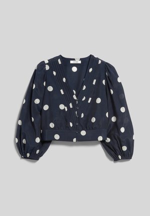 Námornícka modrá krátka blúzka s bielymi bodkami, hlbokým výstrihom do V, zapínaním na gombíky vpredu a dlhými nafúknutými rukávmi s elastickými manžetami.