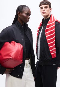 Δύο μοντέλα φορούν μαύρα μπουφάν· το ένα κρατά μια κόκκινη τσάντα, το άλλο έχει ένα κόκκινο και άσπρο ριγέ πουλόβερ περασμένο στους ώμους.