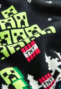 Gehaakte deken met een zwarte achtergrond, heldergroene pixelachtige graphics, rode TNT-blokken en witte sneeuwvlokpatronen. Zachte textuur.