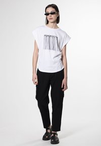 Hvid kortærmet t-shirt med "FASHION VICTIM" grafik, parret med sorte cargo-bukser og kraftige sorte sandaler. Minimalistisk design og afslappet pasform.