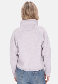 Pullover in morbido pile grigio chiaro, con colletto alto, maniche raglan e vestibilità comoda, abbinato a jeans blu a vita alta.
