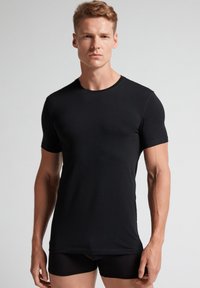 Černé tričko s krátkým rukávem vyrobené z měkkého materiálu, s kulatým výstřihem a přiléhavým střihem. Hladká textura bez viditelných vzorů nebo akcentů.