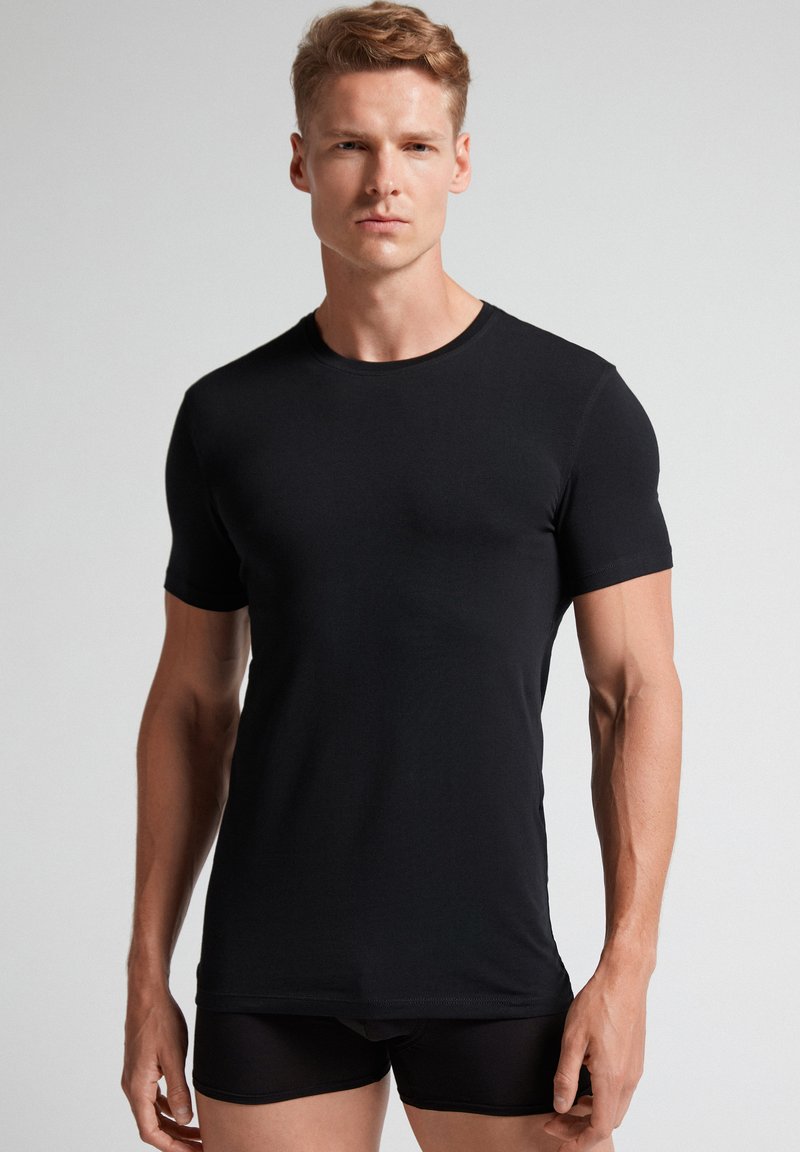 Černé tričko s krátkým rukávem vyrobené z měkkého materiálu, s kulatým výstřihem a přiléhavým střihem. Hladká textura bez viditelných vzorů nebo akcentů.