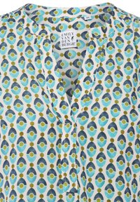 Blouse à manches courtes avec décolleté en V, arborant un motif répétitif d'ovales bleus et verts sur fond blanc. Fabriquée en tissu léger.