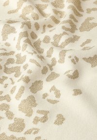 Tessuto con stampa leopardata in crema con accenti dorati metallici, caratterizzato da una superficie texturizzata e da motivi a macchie variabili in tutto il tessuto.