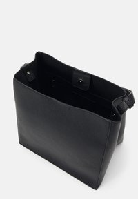 Czarna torebka tote z teksturowanej skóry, z otwartym wierzchem, zapięciem na zatrzask, wewnętrzną kieszenią na zamek i szerokim paskiem na ramię na białym tle.