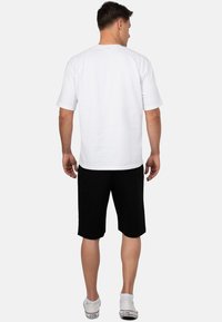 Witte katoenen T-shirt met korte mouwen, gecombineerd met zwarte shorts. Het shirt heeft een ronde hals en een losse fit. Schoeisel bestaat uit witte sneakers.