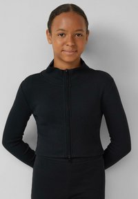 Schwarze gerippte Jacke mit hohem Kragen, durchgehendem Reißverschluss und langen Ärmeln, kombiniert mit passenden Hosen. Weiche Textur und figurbetontes Design.