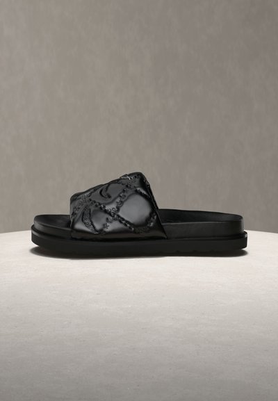 Μαύρο σανδάλι slide με παχιά σόλα και υφασμένο λουράκι με ραμμένα γεωμετρικά σχέδια, εμφανίζεται σε προφίλ πλάγιου μέρους σε ουδέτερο φόντο.