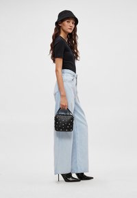 Černé přiléhavé tričko, světle modré džínové kalhoty s širokými nohavicemi a vysokým pasem, černá kabelka s cvočky, černé lodičky na jehlovém podpatku a černý žebrovaný klobouk typu bucket.