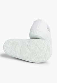Sneaker bianca in tela con suola in gomma testurizzata, caratterizzata da un design piatto e un branding minimale sul tallone.