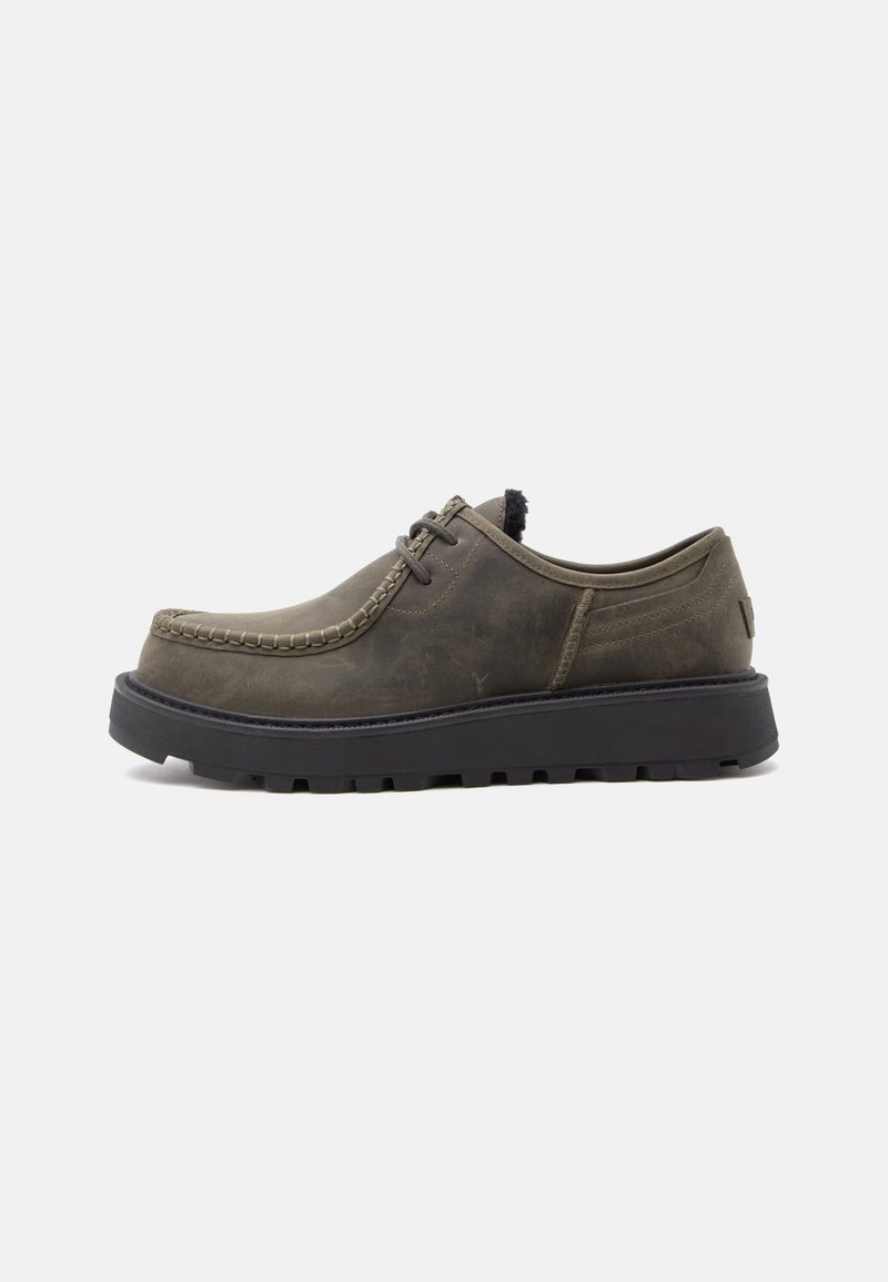 Chaussure en cuir vert olive foncé à lacets avec semelle noire épaisse et couture style mocassin le long du bout, présentée en profil latéral sur fond blanc.