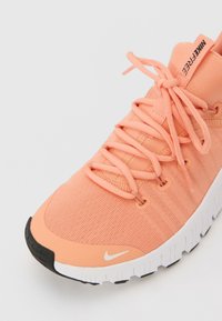 Scarpa da ginnastica Nike color pesca con tessuto strutturato, suola intermedia a contrasto e sistema di allacciatura prominente. Punta curva e logo del marchio sulla linguetta.