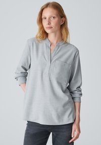 Camicia a maniche lunghe grigio chiaro con colletto a band, tasca frontale e texture morbida. Stilizzata con maniche a risvolto e vestibilità rilassata.
