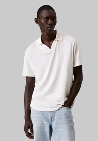 Lichtbeige polo shirt met een gestructureerde afwerking, korte mouwen en een V-hals. Gecombineerd met lichtblauwe denim jeans.