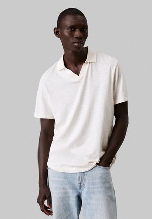 Lichtbeige polo shirt met een gestructureerde afwerking, korte mouwen en een V-hals. Gecombineerd met lichtblauwe denim jeans.
