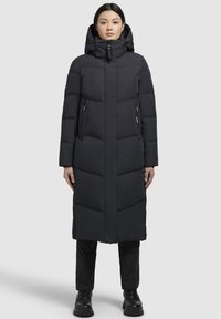 Abrigo de plumas negro largo con capucha, que presenta un cierre con cremallera en la parte delantera, diseño de costillas verticales y dos bolsillos laterales con cremallera. Textura suave.