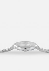 Reloj de pulsera plateado con una caja redonda, esfera clara y un bisel engastado de joyas. Presenta una pulsera de metal con un patrón y una corona a presión marcada como "LJ."