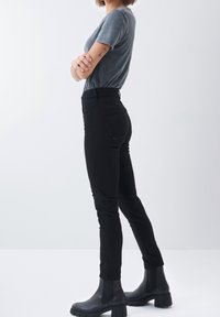 Pantalones negros ajustados de denim con una textura suave. Combinados con una camiseta gris de manga corta y botines negros gruesos.
